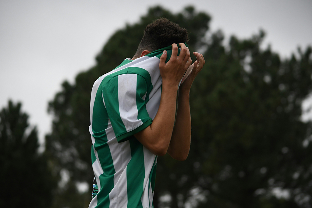 Voetballer baalt en trekt zijn groen/witte voetbalshirt over zijn hoofd.