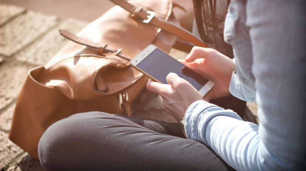 Jonge vrouw zittend op de grond, met in haar handen een smartphone