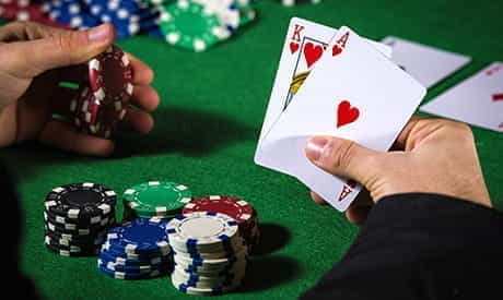 a king of clubs and an ace of clubs in a players hand with casino chips on a green felt table.