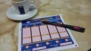 A EuroMillions lottery slip, pen and a cup of coffee.