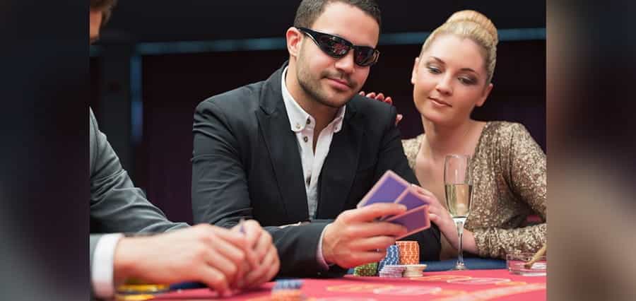 A casino player with playing cards, and a woman looking at his cards.