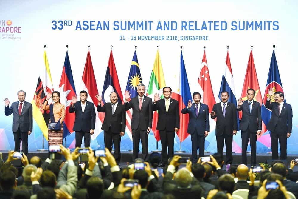 ASEAN nation leaders stand on a stage and wave at 2018 ASEAN summit.
