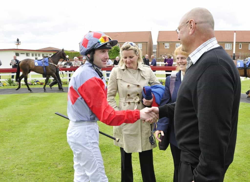 Jockey Robert Winston shakes hands with Alan Cairns among other horse racing professionals.