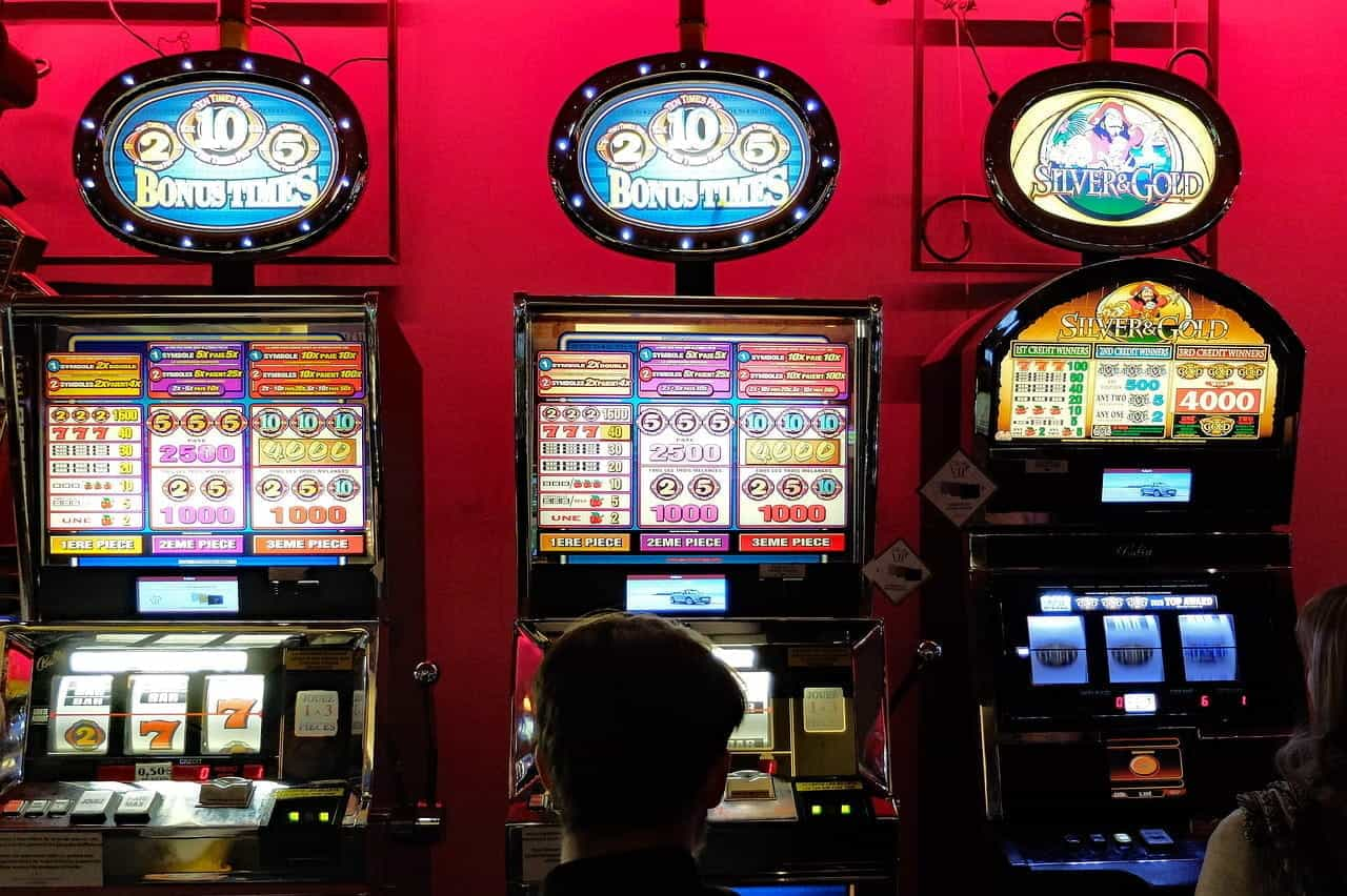 Three slot machines against a red wall in a casino.