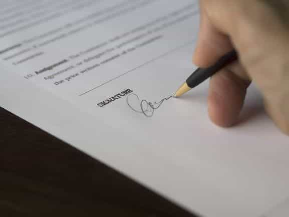 A white hand signs a contract.