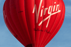 A Virgin red hot air balloon in a bright blue sky.