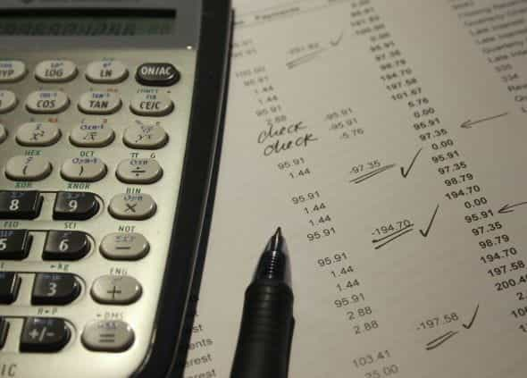 A close-up of a calculator and paper demonstrating lines of expenses.