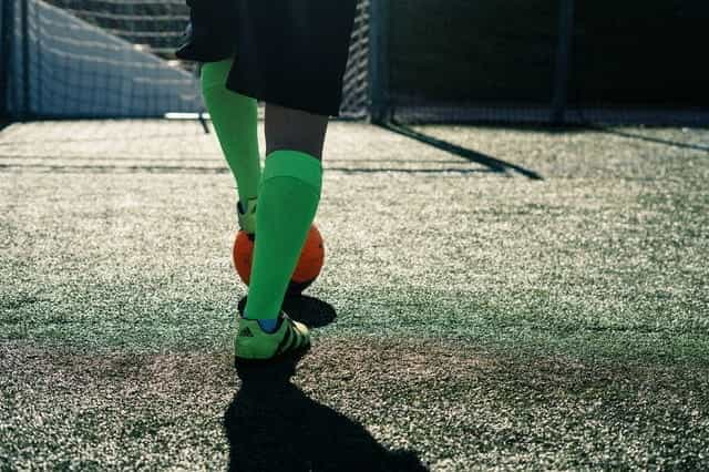 A footballer in green socks and boots, with foot on orange ball.