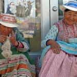 Two older women sit on a stoop in Chivay, Peru wearing traditional costumes.