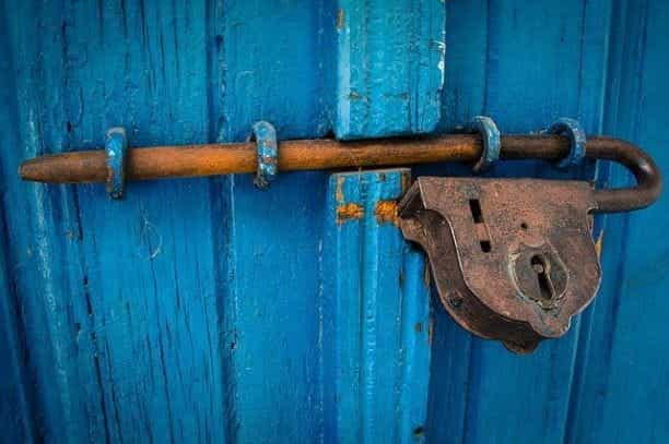 A blue wooden door secured shut thanks to a bolt and padlock.