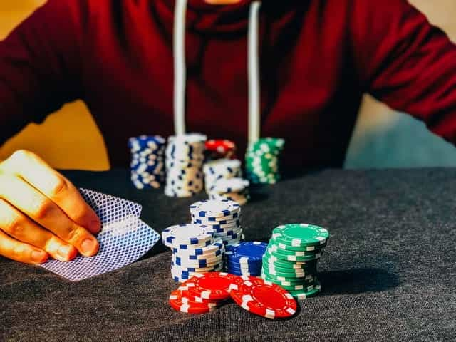 A person sitting in front of several stacks of poker chips while peeking at his cards.