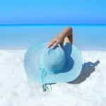 A woman lying on a beach with a blue hat.