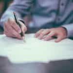 Hands sign paperwork at a desk.