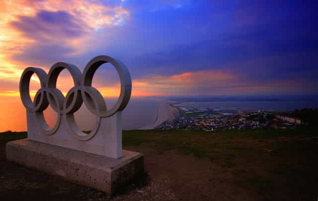 Olympic rings statue overlooking the sea and a city.