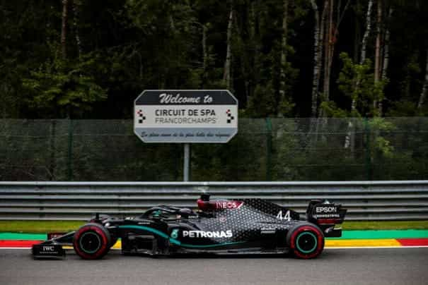 A Mercedes F1 car passes a Circuit De Spa road-sign at high speed.