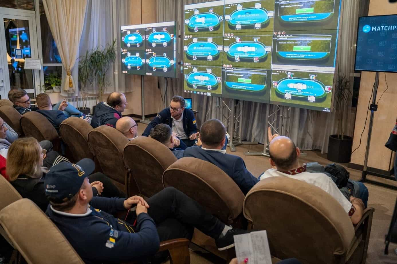 Spectators watching a bank of screens displaying animated poker tables.