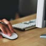 A person holding a computer mouse, working with a monitor and keyboard.