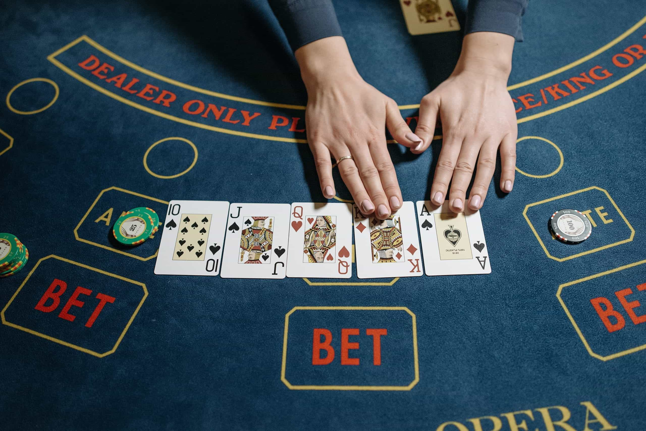 Five playing cards laid out on gaming table with hands touching a King and an Ace.