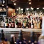 The wall behind a bar, filled with rows and rows of alcohol in bottles.