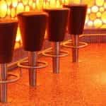 Four fixed barstools at a bar with a lit-up pattern design running along the side of the bar.