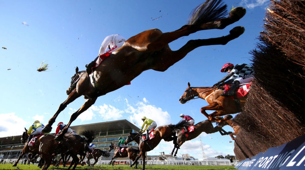 Horses clearing a chase obstacle at Newbury Racecourse.