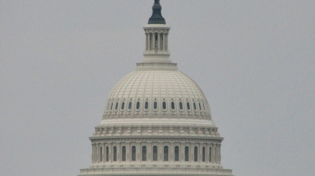 The United States Capitol dome rising over a hill.